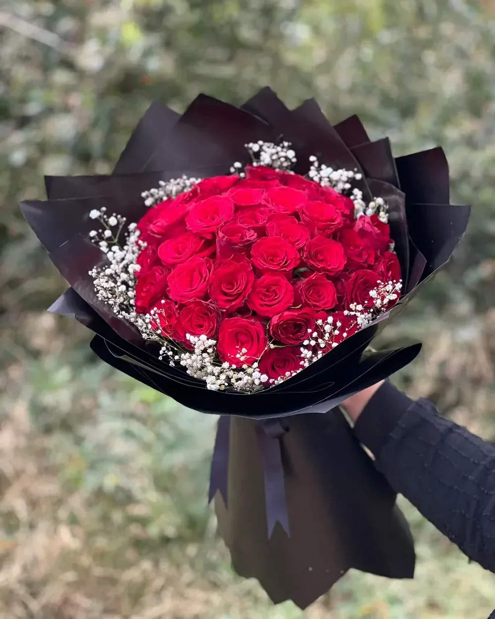 Siyah kağıda sarılı kırmızı gül buketi, elde tutuluyor